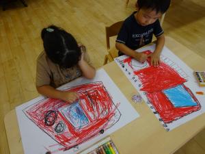机の上で消防車の色を塗りこむ４歳児。